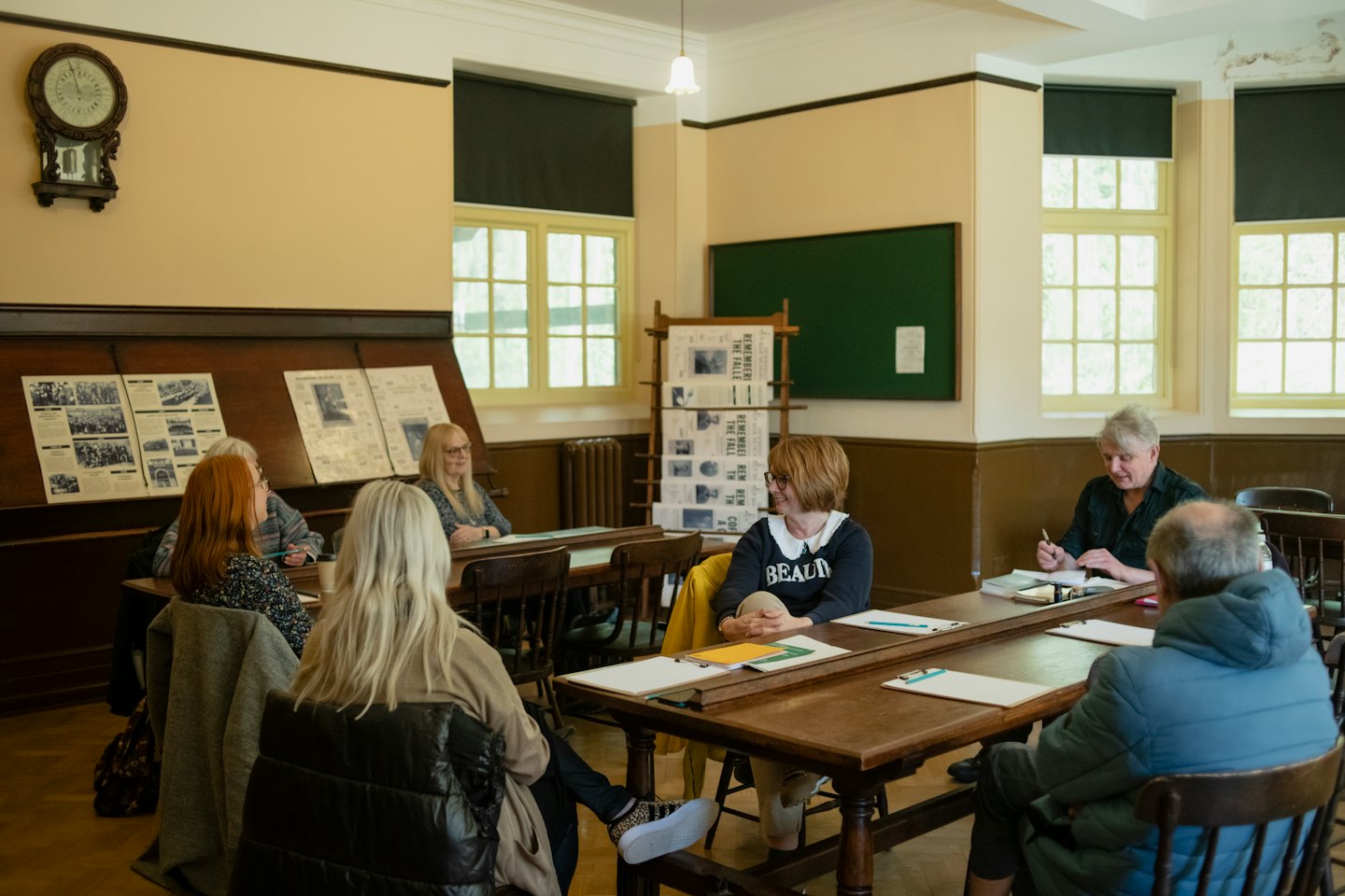Adulti che discutono a tavoli di legno in un'aula d'altri tempi.
