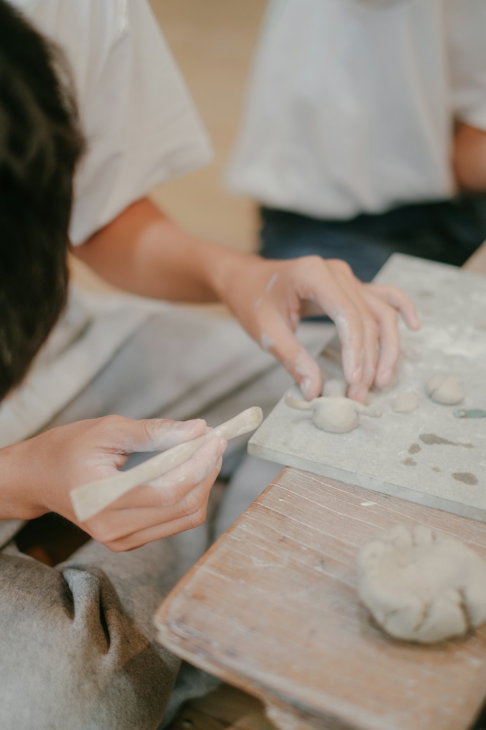 Due mani modellano argilla su un tavolo di legno.