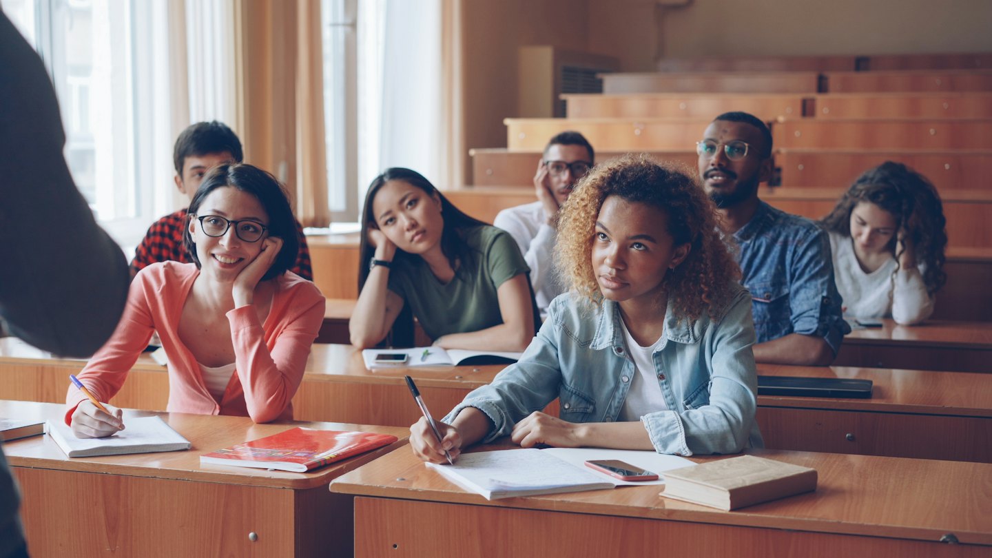 Un gruppo eterogeneo di studenti ascolta e prende appunti in un'aula magna.